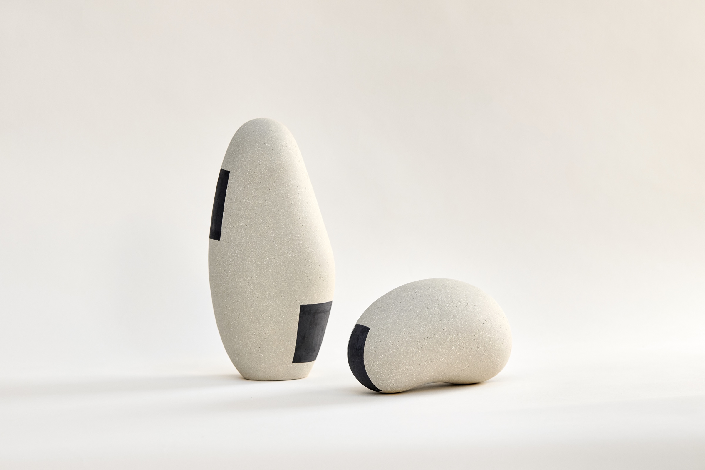 Deux sculptures Ishi : grand ovoïde vertical et galet incliné en porcelaine et grès, décor géométrique d'oxydes noirs, façonnage main au colombin