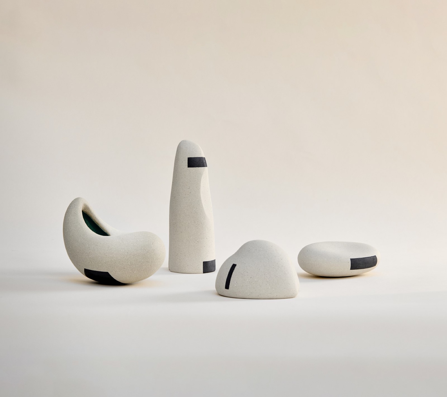 Quatre sculptures céramiques de la série Ishi par Azami Ballart Kobayashi. Porcelaine et grès façonnés à la main, décor géométrique d'oxydes noirs, émail bleu à l'intérieur des formes ouvertes