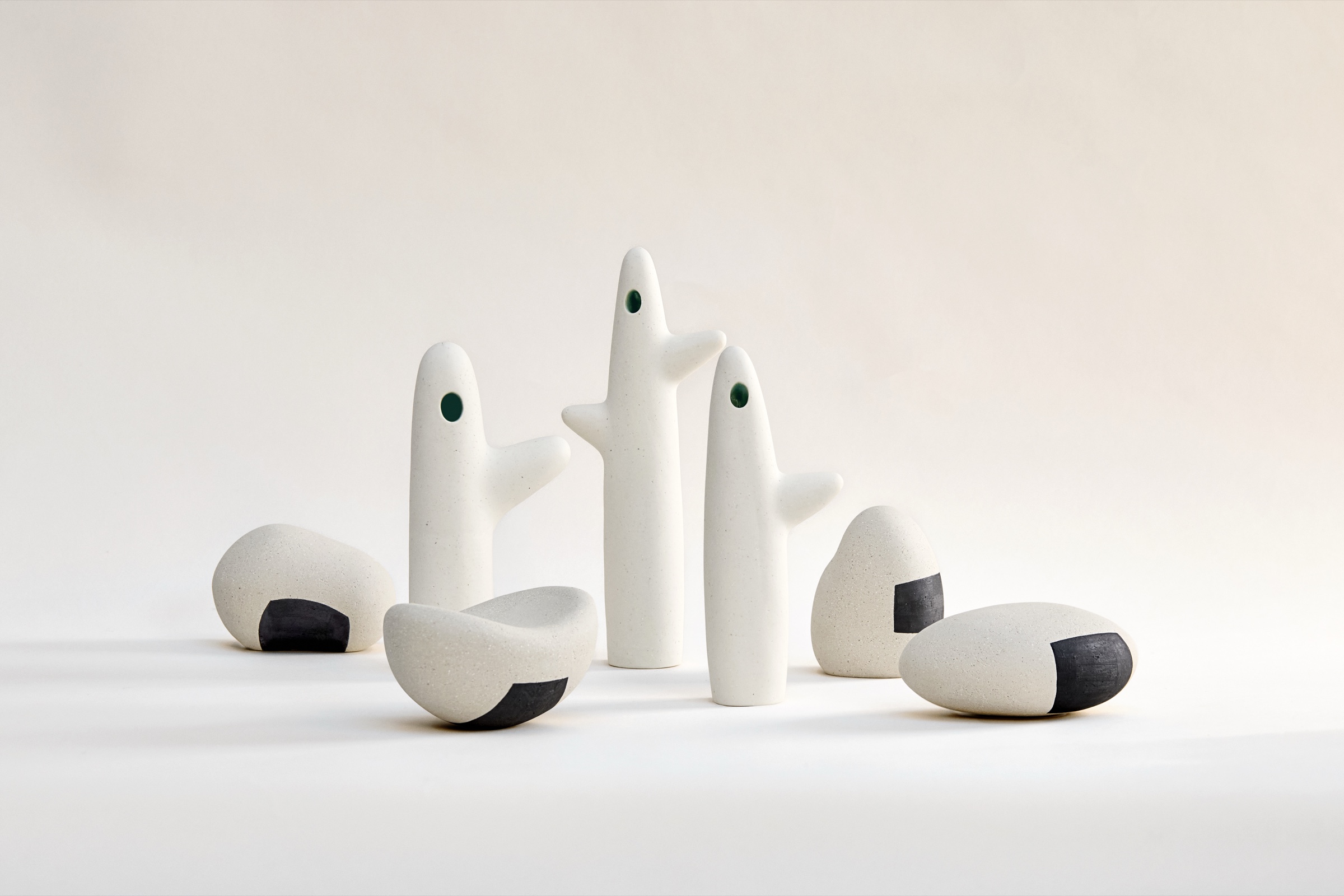 Sculptures céramiques Azami Ballart Kobayashi, séries Koboku et Ishi : trois totems Koboku en grès blanc aux silhouettes minimalistes ponctuées d'une ouverture ronde, et trois galets Ishi au décor d'oxydes noirs